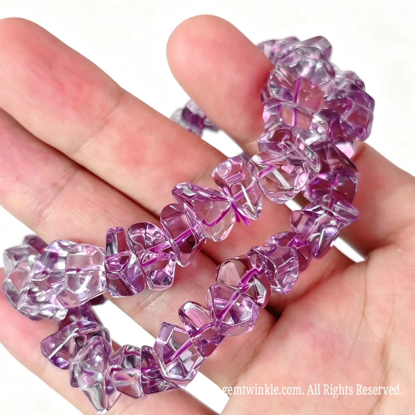 Amethyst chip stretch bracelets with approx 10mm polished pebbles laid across open hand highlighting rich violet tones