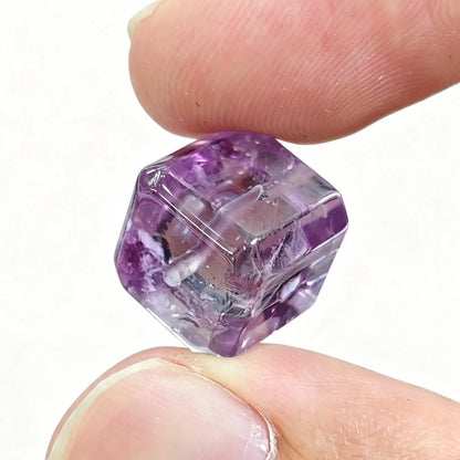 Fingers holding a purple amethyst sugar cube bead showing center drill hole and bevel edges
