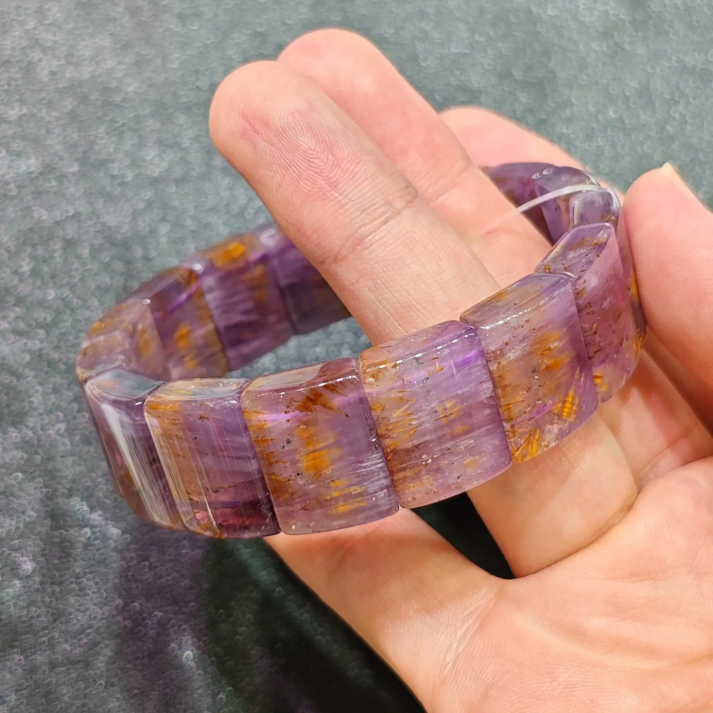 Hand holding amethyst rutilated quartz bangle showing golden copper rutile needles in purple crystal under light