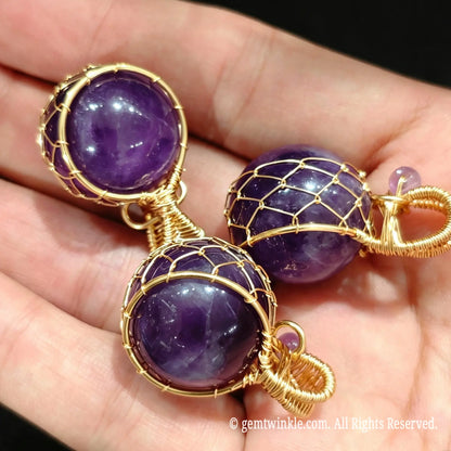 Three gold wire wrapped amethyst sphere pendants resting on palm showing rich purple color and wire mesh detail