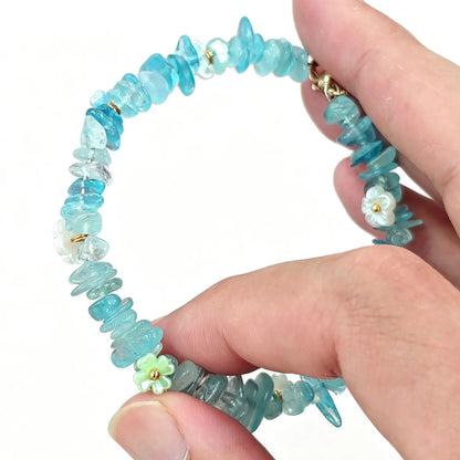 Aquamarine chips bracelet strung on metal wire held in hand featuring 5-10mm blue gravel beads and flower accents