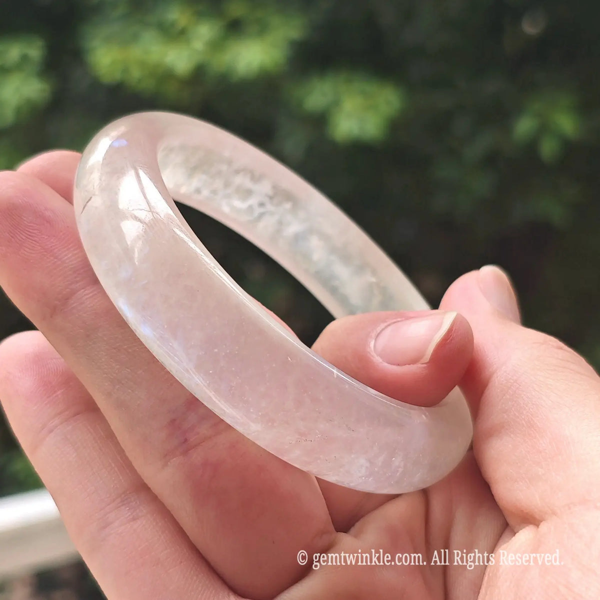 Designer hand displaying the translucent crystal quality and glowing blue light of a moonstone bangle