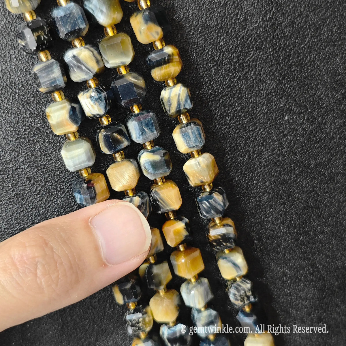 Designer hand holding dreamy tiger eye gemstone strands to demonstrate bead scale and polished luster