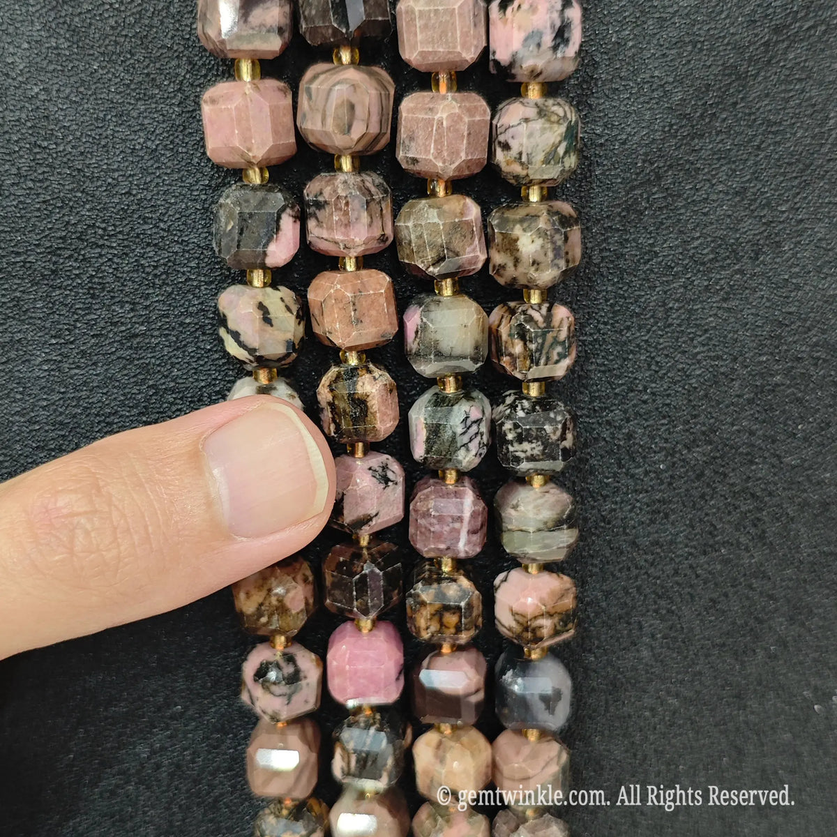 Designer hand holding rhodonite gemstone strands to demonstrate bead scale and polished luster