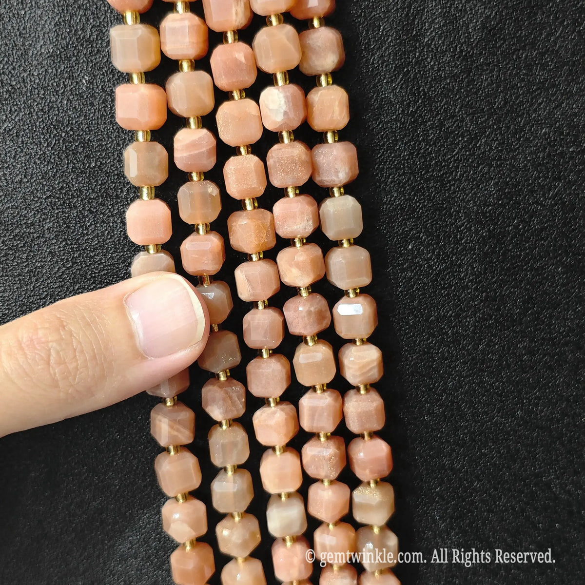 Designer hand holding sunstone gemstone strands to demonstrate bead scale and polished luster