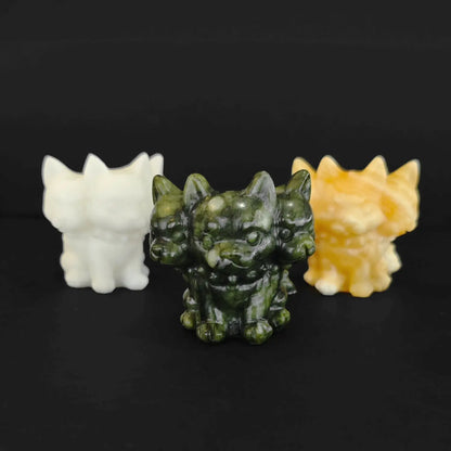 Three cute natural gemstone Cerberus figurines with three heads carved from white marble yellow calcite and green serpentine standing together on a black background
