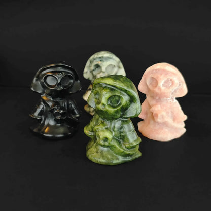 Four cute natural gemstone Grim Reaper figurines holding scythes standing together on a black background