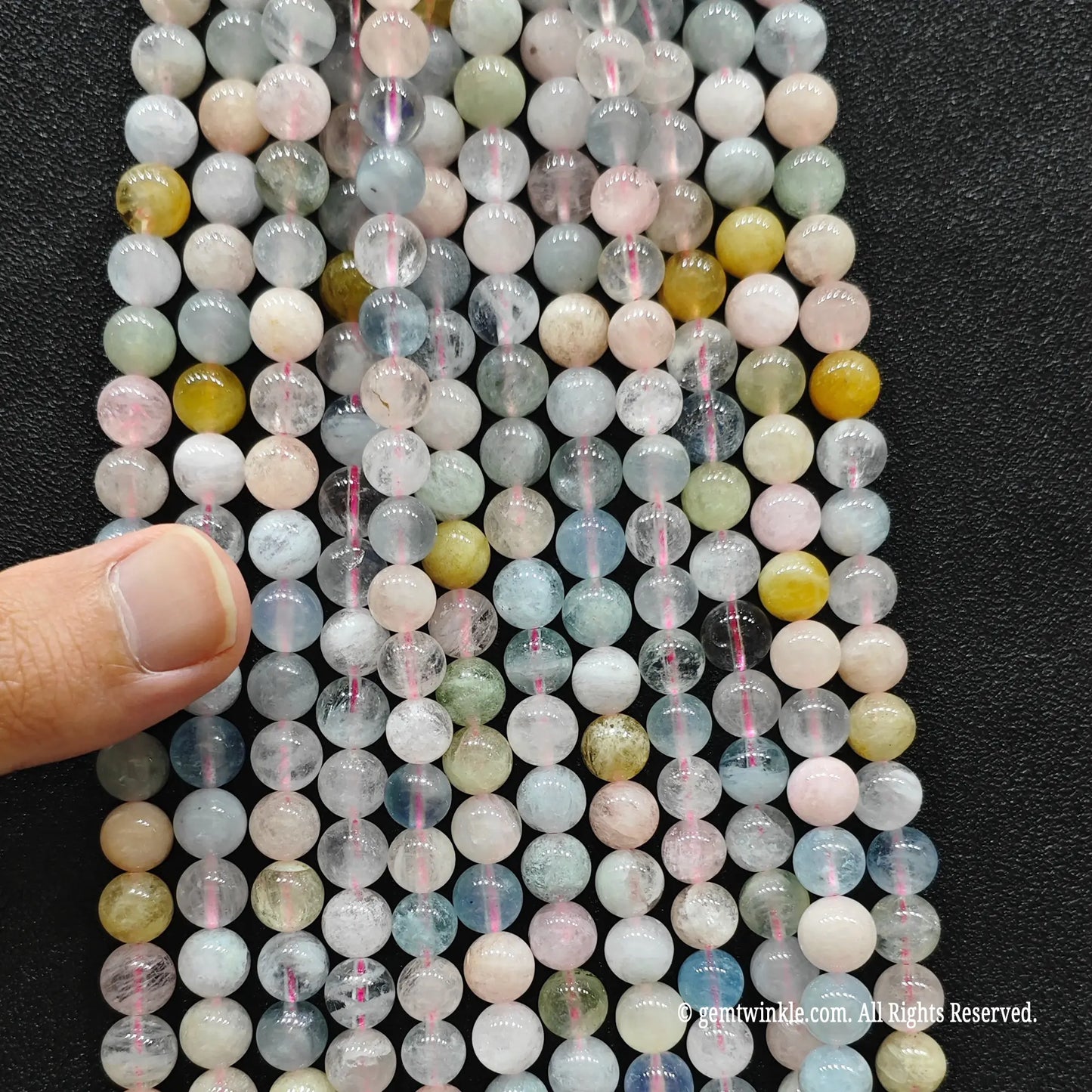 Hand holding multiple strands of B plus commercial grade multi color morganite crystal beads to inspect the 4mm to 8mm size chart distribution