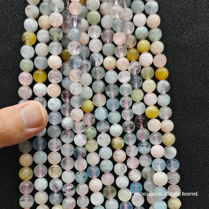 Hand holding multiple strands of B plus commercial grade multi color morganite crystal beads to inspect the 4mm to 8mm size chart distribution