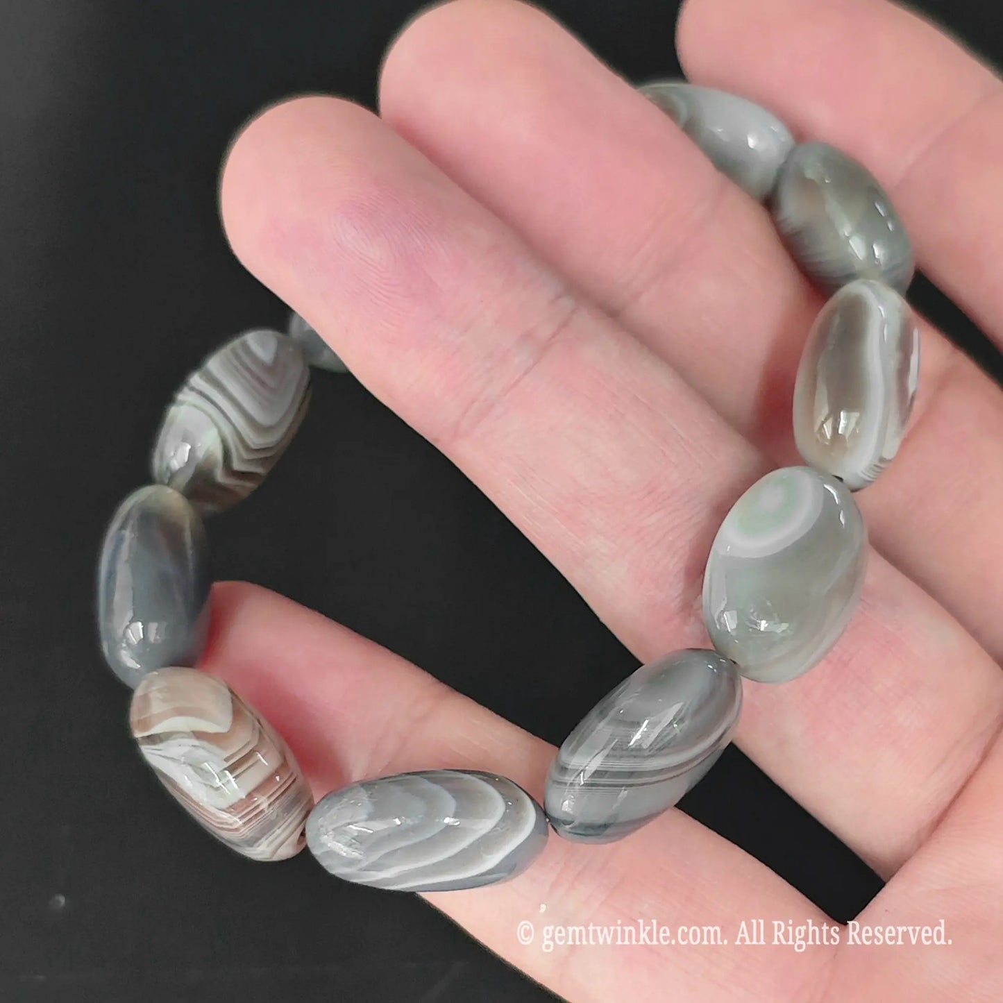 banded grey agate oval bead strand laid flat across fingers