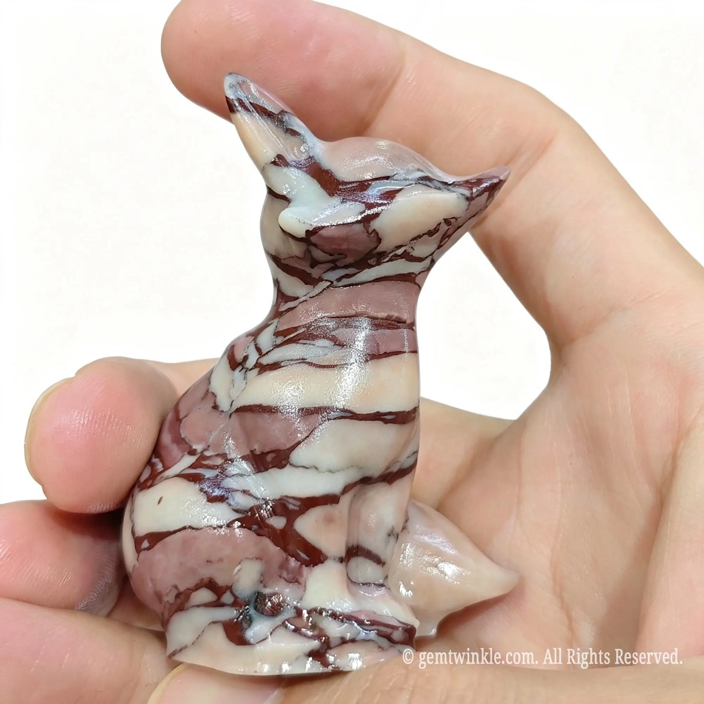 Side view of banded jasper fox carving held in hand highlighting seated pose and tail texturing