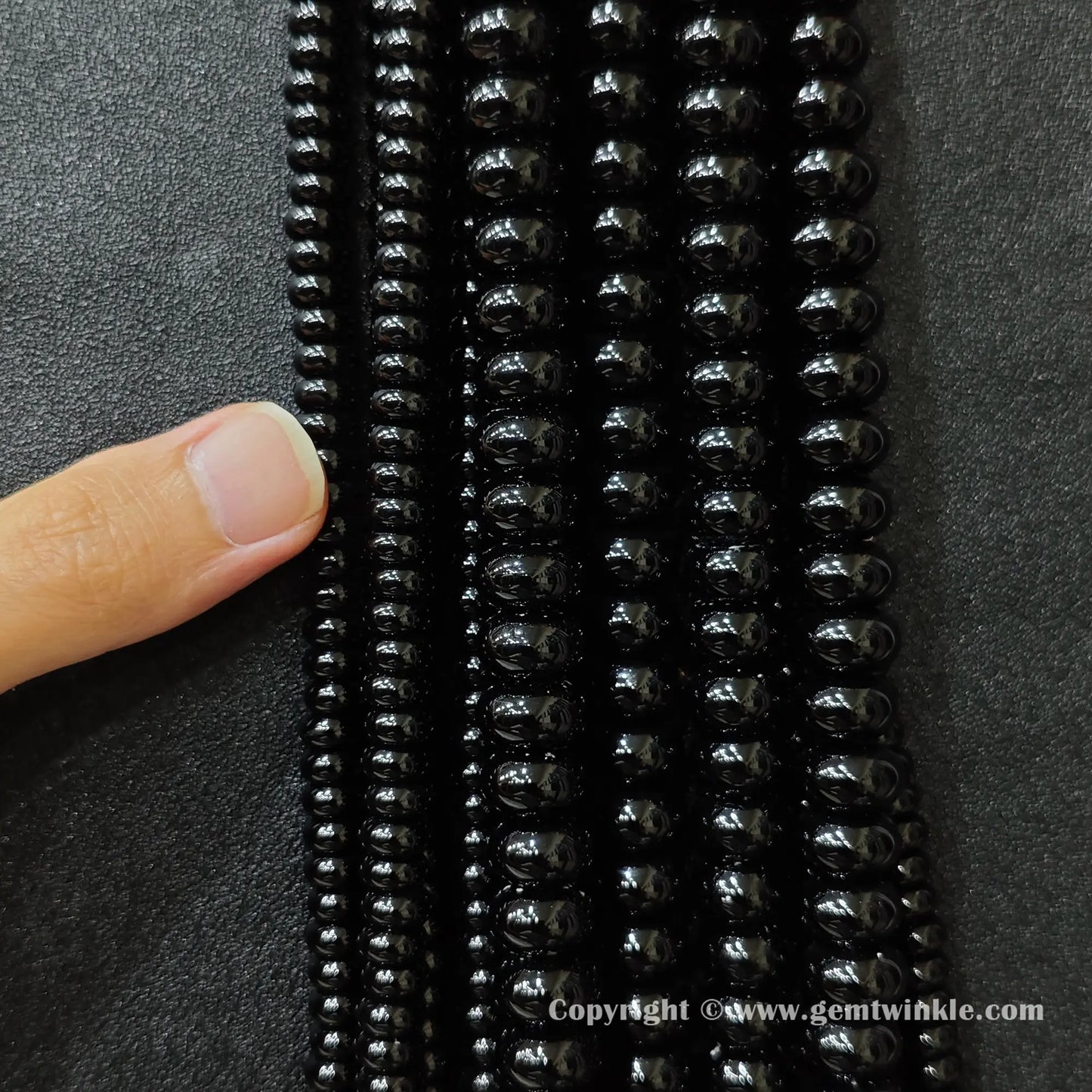 Close up view of black agate smooth disc rondelle beads inspected on fingers for quality preview