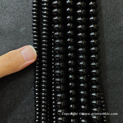 Close up view of black agate smooth disc rondelle beads inspected on fingers for quality preview