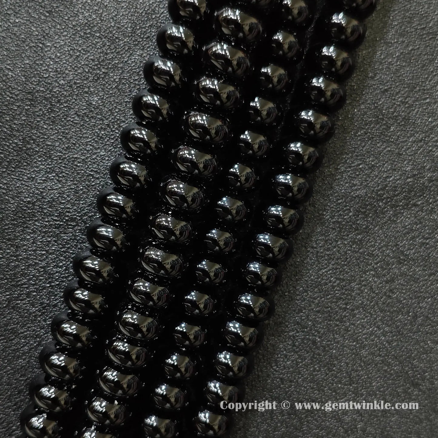 Angled view of color dyed black agate smooth disc gemstone strands arranged parallel on dark background