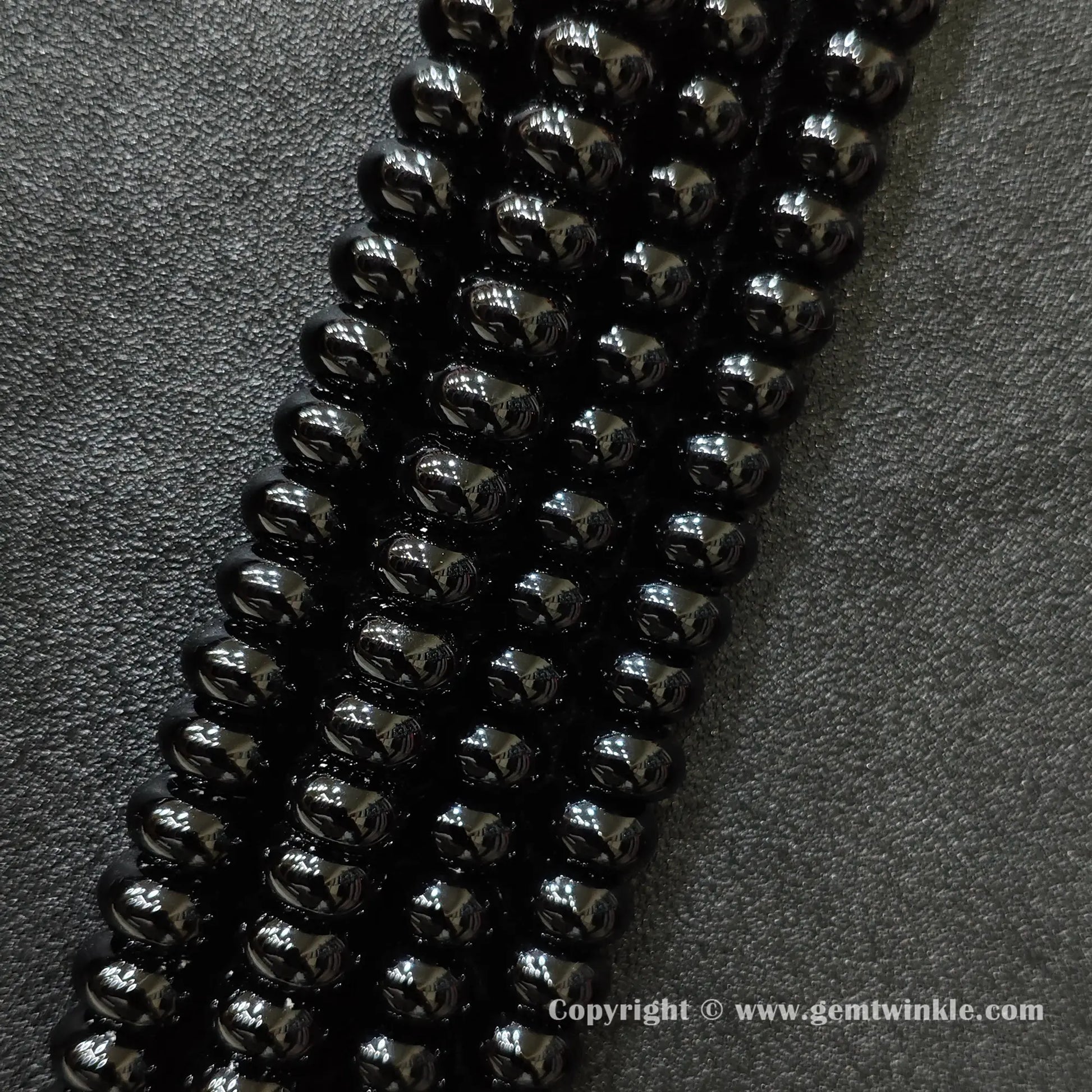 Angled view of color dyed black agate smooth disc gemstone strands arranged parallel on dark background