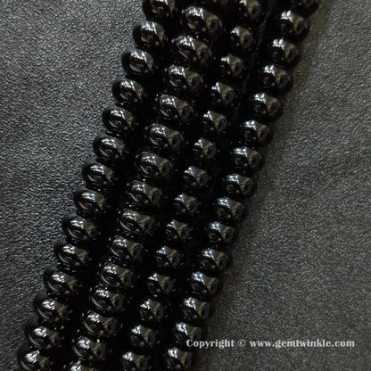 Angled view of color dyed black agate smooth disc gemstone strands arranged parallel on dark background