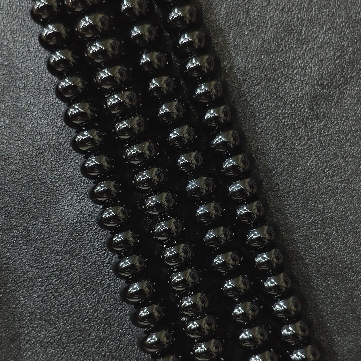 Macro closeup of color dyed black agate smooth rondelle beads in multi size strands with high gloss finish