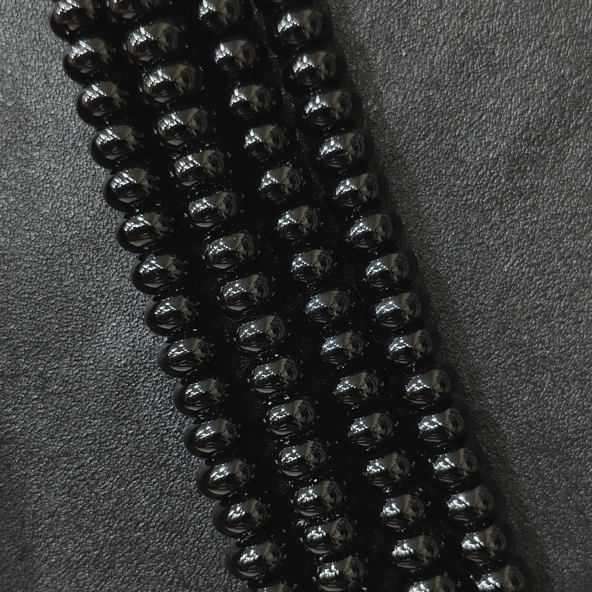 Macro closeup of color dyed black agate smooth rondelle beads in multi size strands with high gloss finish