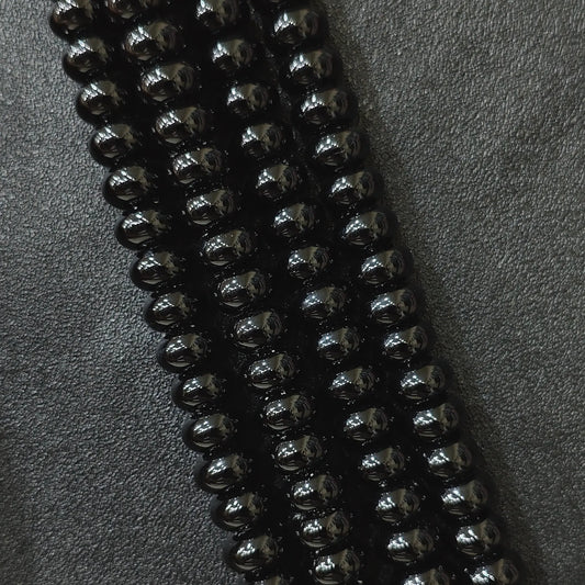 Macro closeup of color dyed black agate smooth rondelle beads in multi size strands with high gloss finish