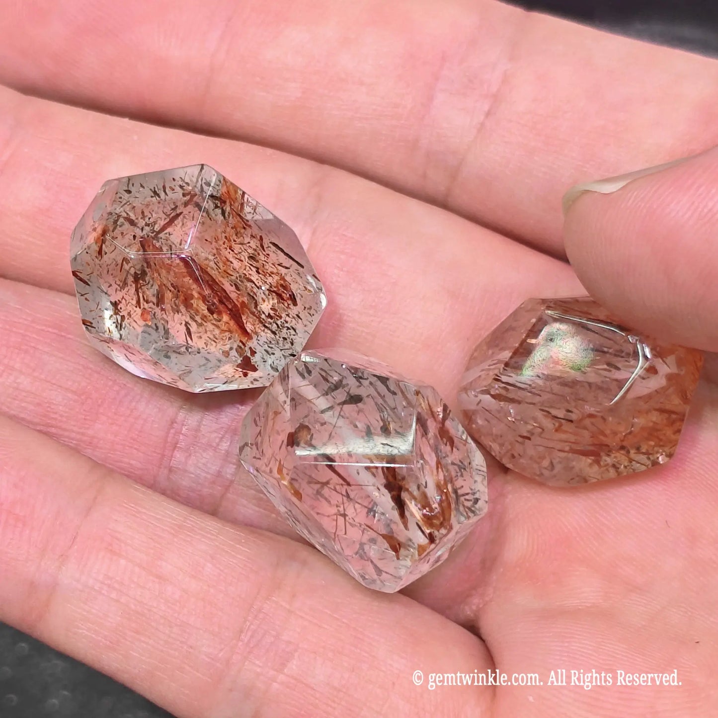 Handheld view of three black gold super seven asymmetrical faceted beads showing dense rutile and mica inclusion patterns
