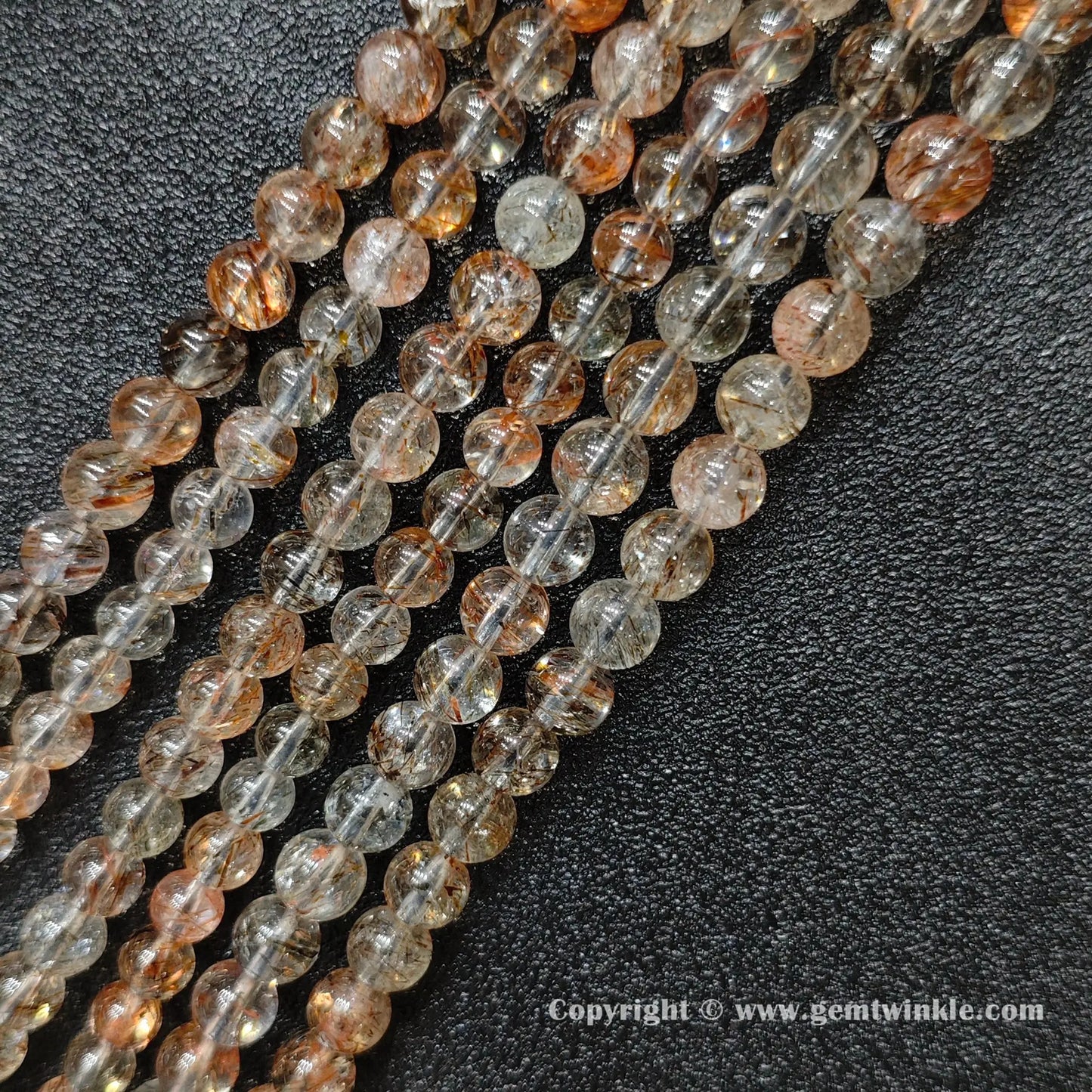Angled view of Grade B black gold super seven round bead strands laid parallel on dark surface