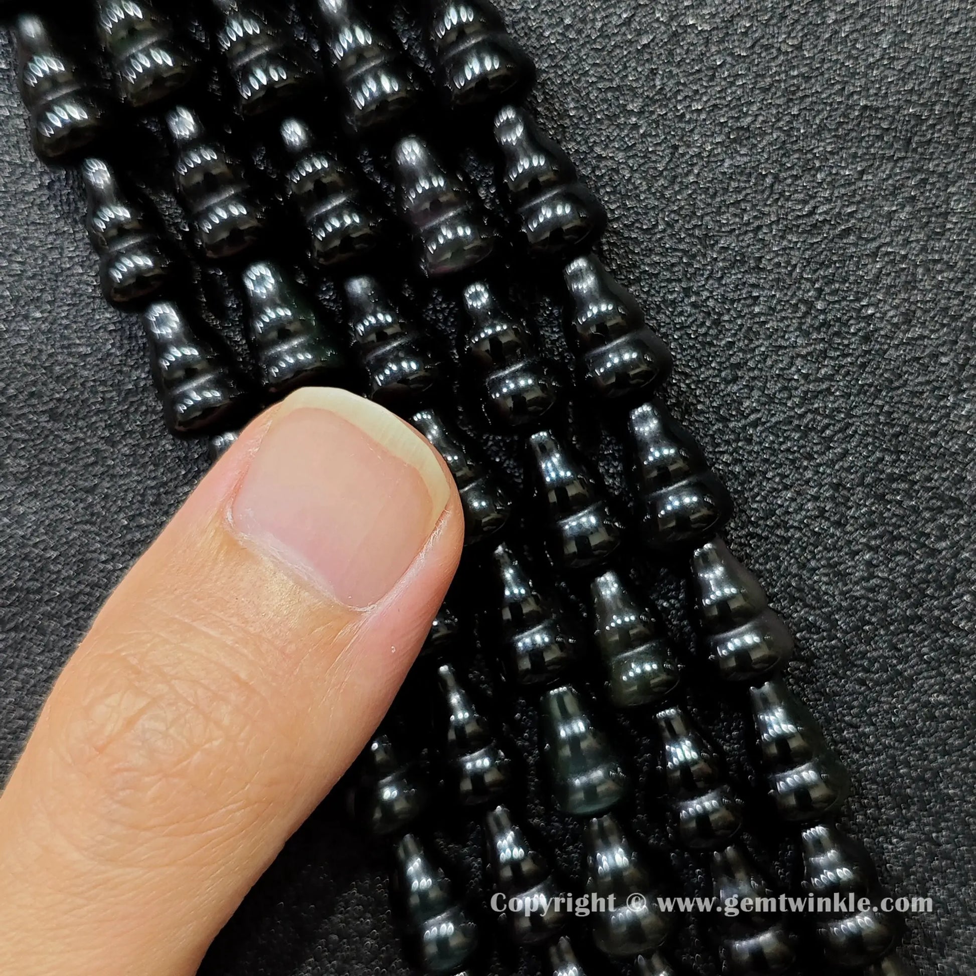 Close up view of natural black obsidian calabash beads held on fingers for quality preview