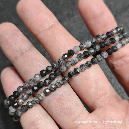 Multiple 4mm black rutilated quartz faceted bead bracelets laid across hand demonstrating monochrome contrast and stretch fit