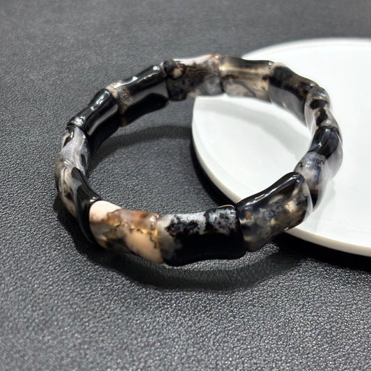 Close up of black sakura agate bamboo bracelet displayed on a white plate.