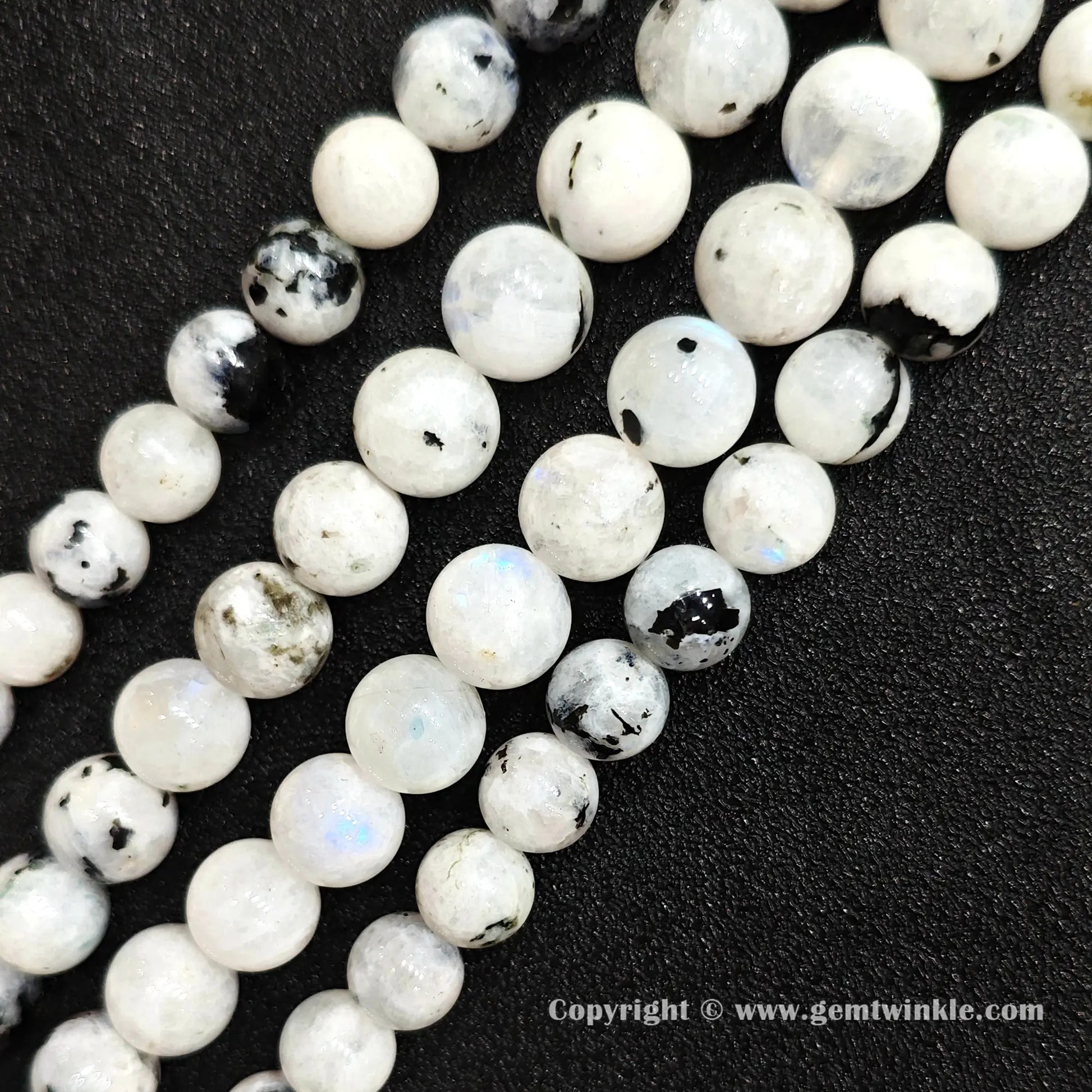 Angled view of black spotted blue flash moonstone bead strands displaying blue adularescence on dark backdrop