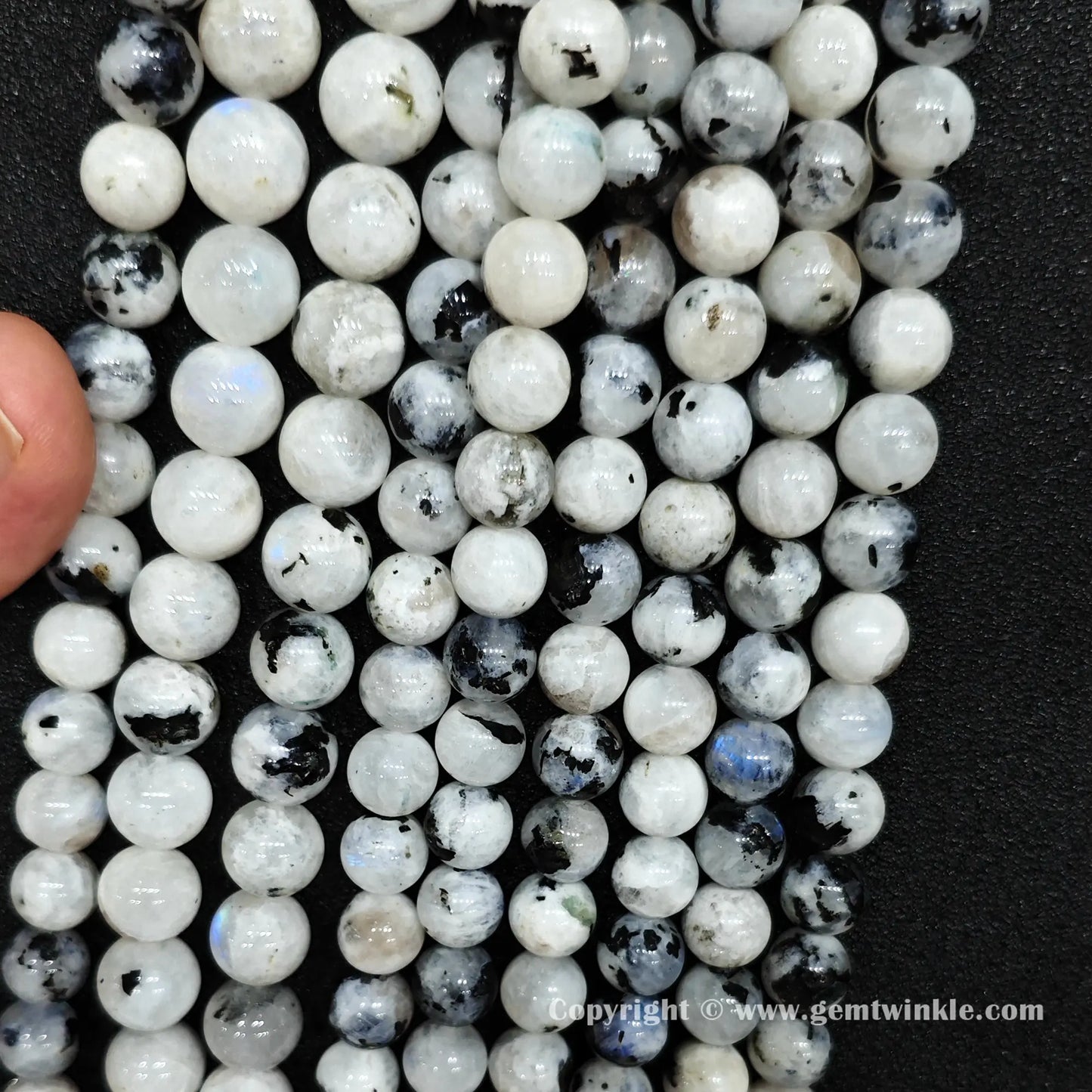 Close up view of black spotted blue flash moonstone round beads held on fingers for natural optical preview