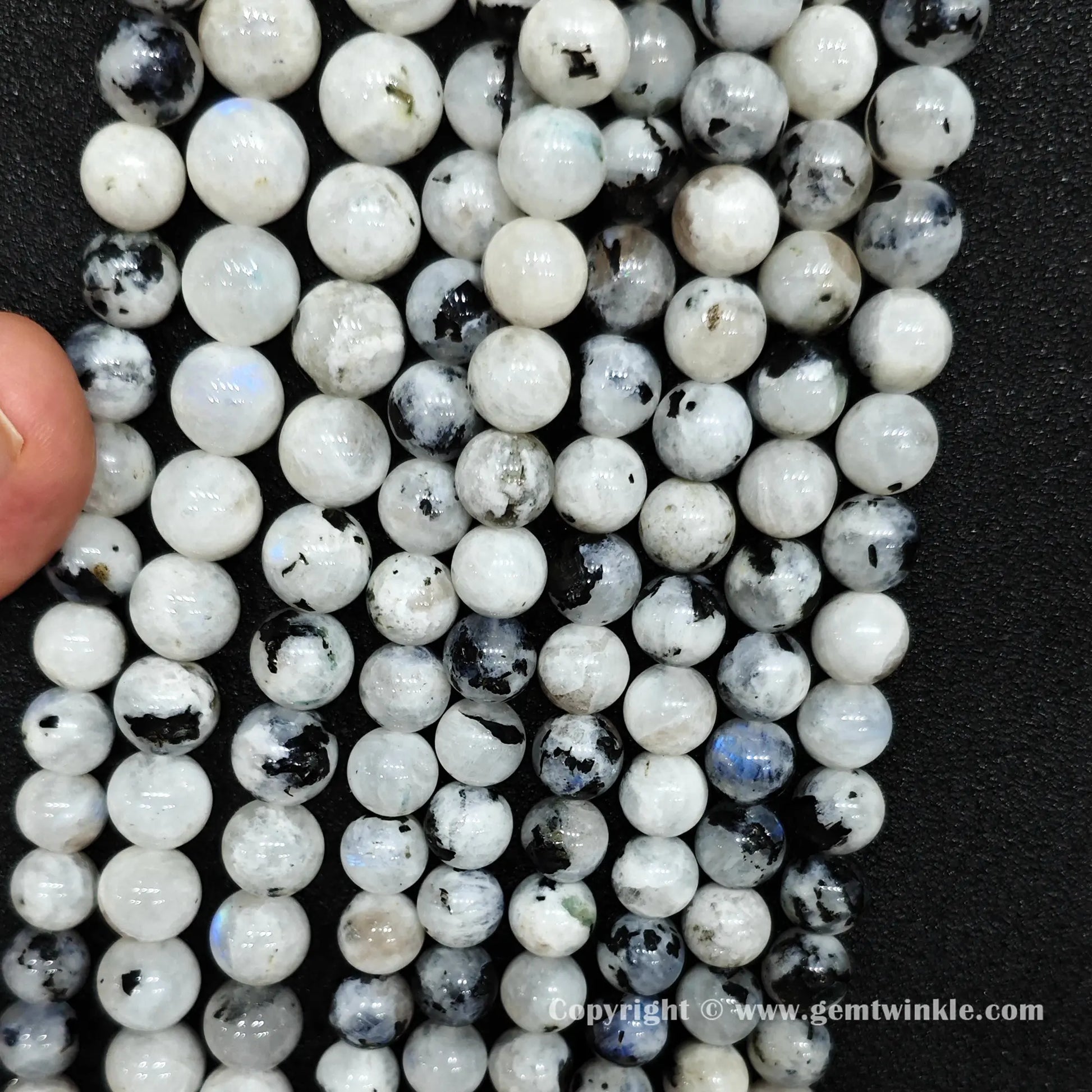 Close up view of black spotted blue flash moonstone round beads held on fingers for natural optical preview