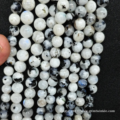 Close up view of black spotted blue flash moonstone round beads held on fingers for natural optical preview