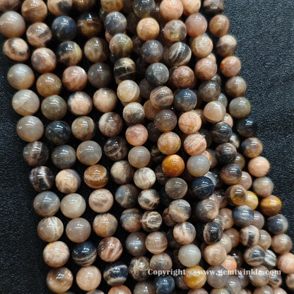 Close up view of natural black sunstone round beads inspected on fingers for quality preview