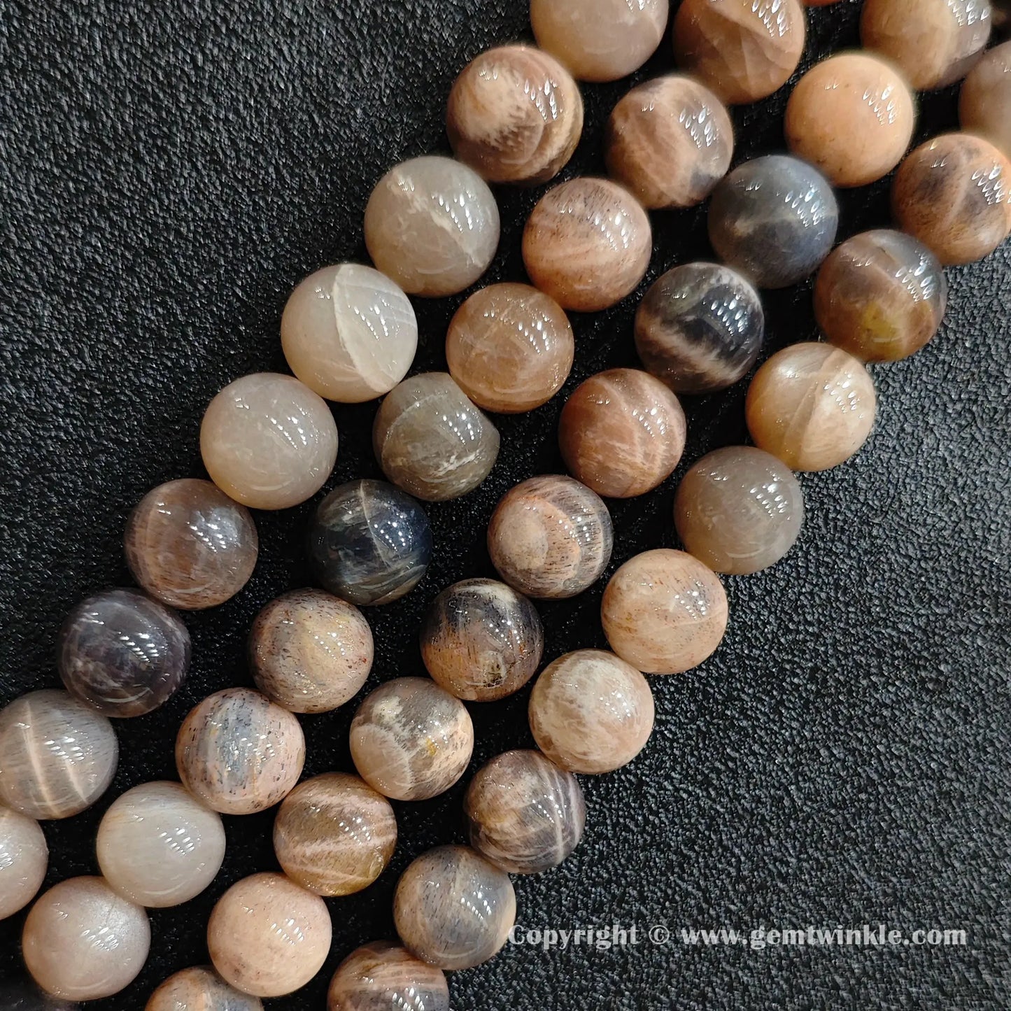 Angled view of natural dark feldspar black sunstone strands arranged parallel on dark background