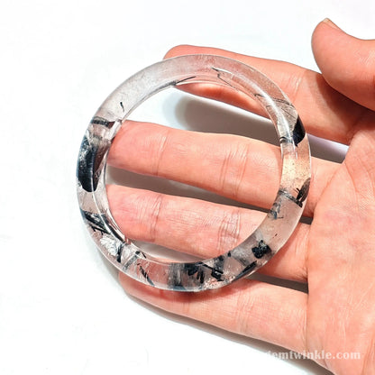Handheld perspective displaying polished black tourmalinated quartz bracelet transparency and size
