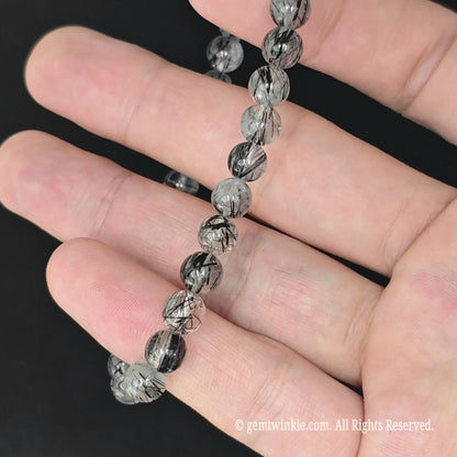 translucent black tourmaline in quartz stretch strand held in hand