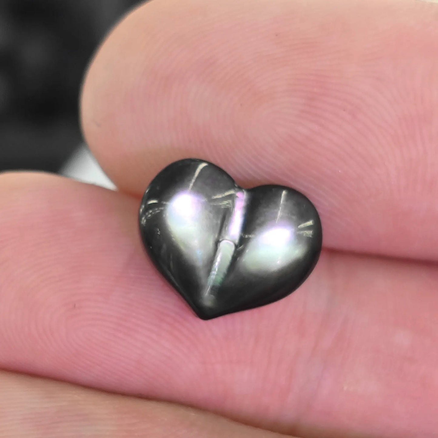 Black lip shell 12mm puffy heart bead held in fingers showing dark mother of pearl peacock iridescence
