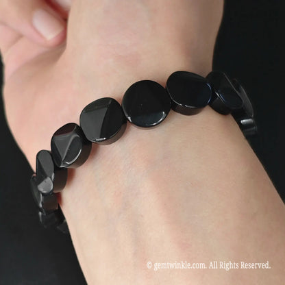 Black obsidian 12mm triangle facet coin bead stretch bracelet styled on wrist displaying lustrous black geometric finish