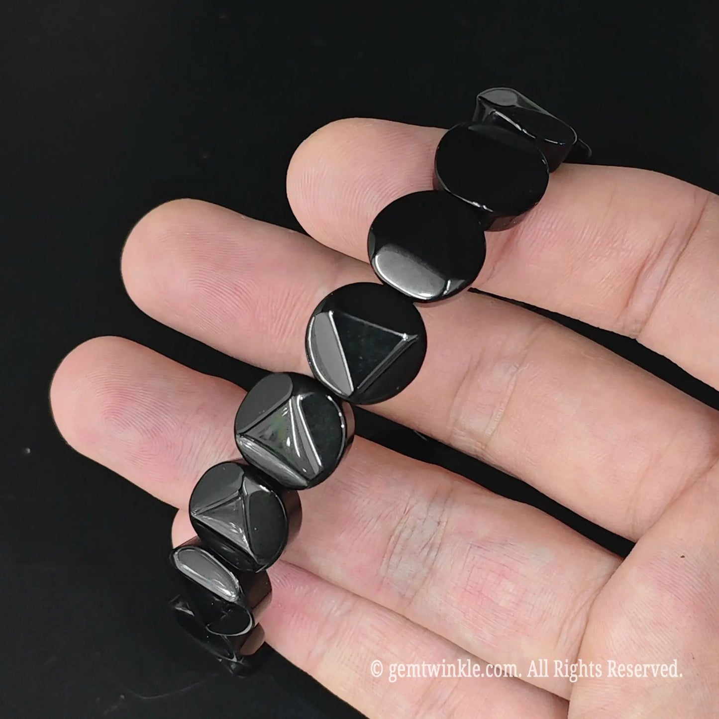 Black obsidian center triangle faceted disc bead bracelet laid across fingers showing uniform geometric bead alignment