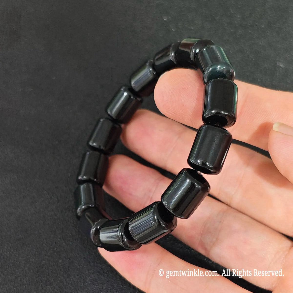 side view of natural black obsidian drum bead stretch bracelet on hand displaying high sheen