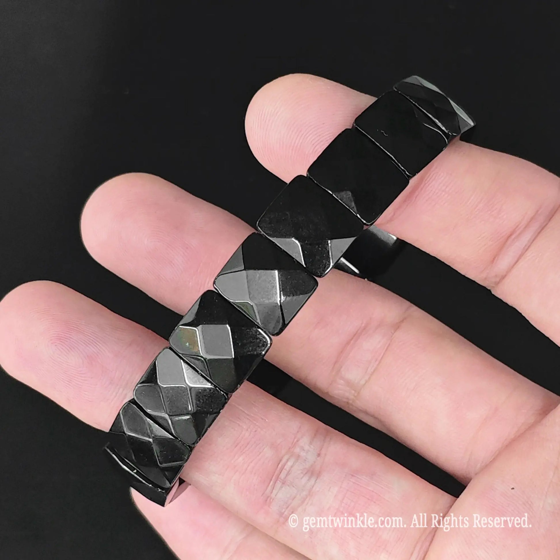 Black obsidian faceted square cuff bracelet displayed across fingers revealing uniform diamond faceting