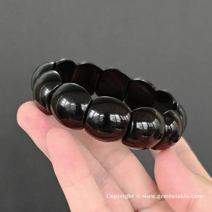 black obsidian plate bangle bracelet resting on hand showing glossy dark texture and stretch cord