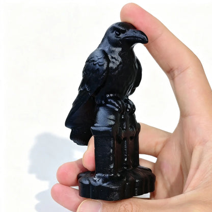 Black obsidian raven statue perched on tombstone base held in hand showing detailed head and beak profile