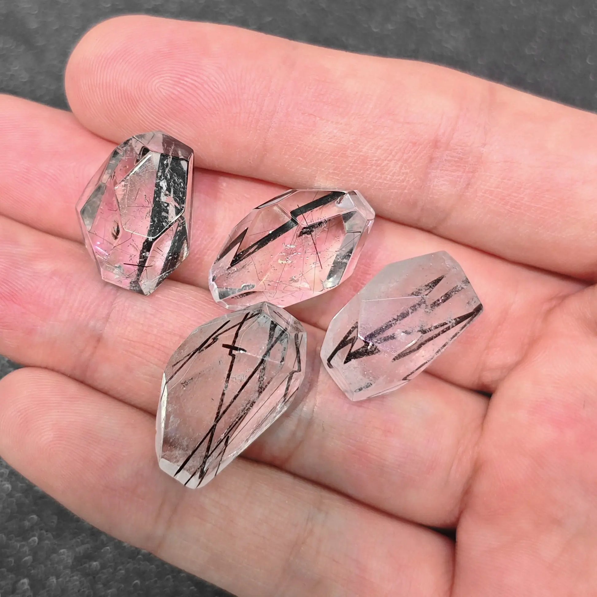 four 20mm black rutilated quartz irregular faceted beads displayed together in palm