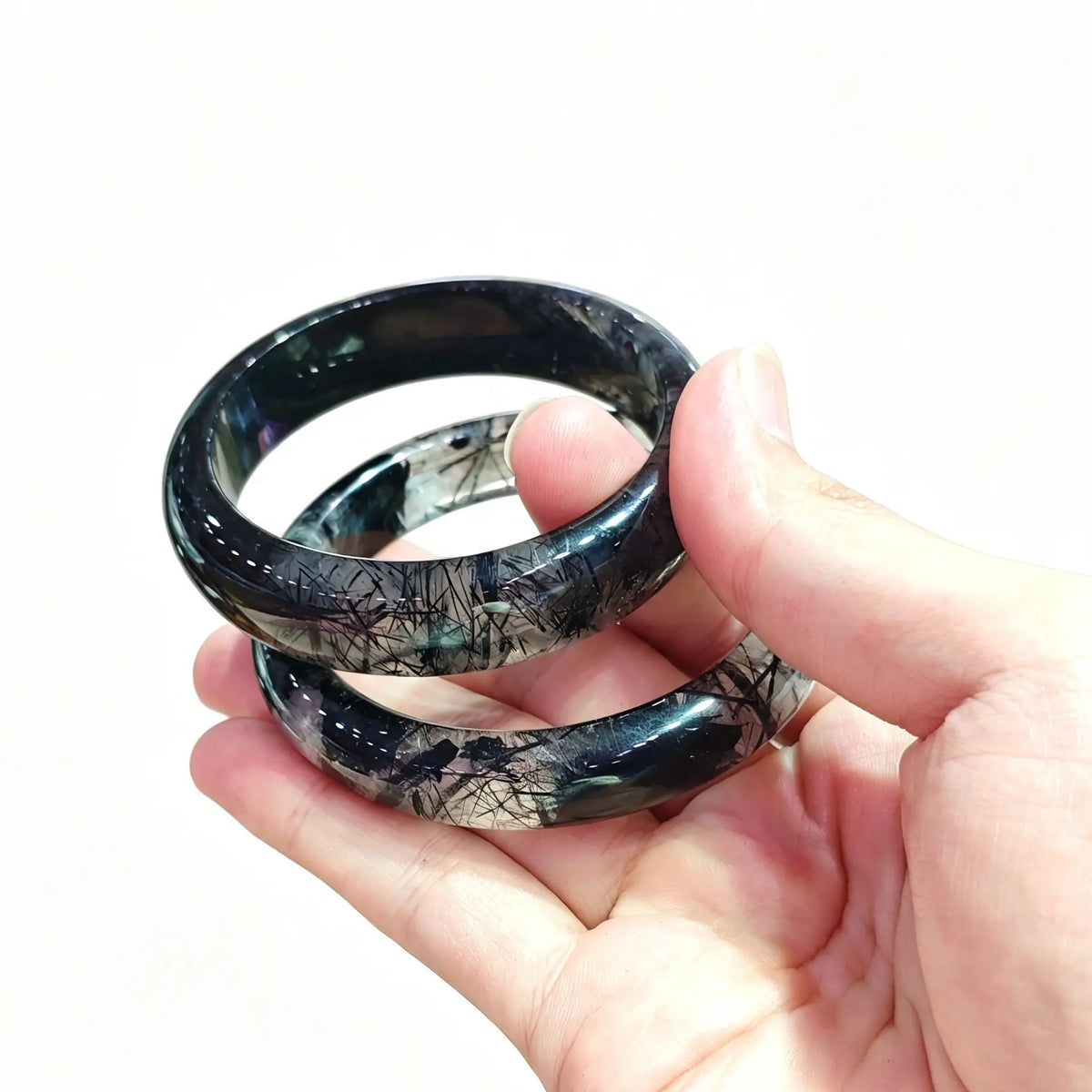 Hand holding black rutilated stone bangles showcasing quality grade tiers and small order inventory options