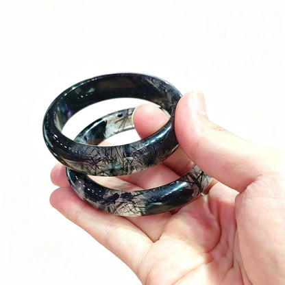 Hand holding black rutilated stone bangles showcasing quality grade tiers and small order inventory options