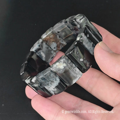 Overview of black sakura agate geometric rectangle plate bracelet held in open palm showing uniform plate bead alignment