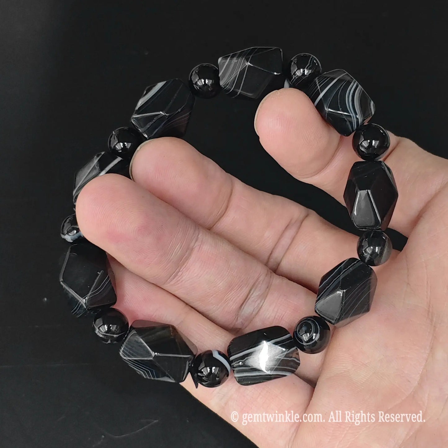 Angle view of black sardonyx 15mm faceted geometric bead bracelet highlighting light reflection across geometric facets