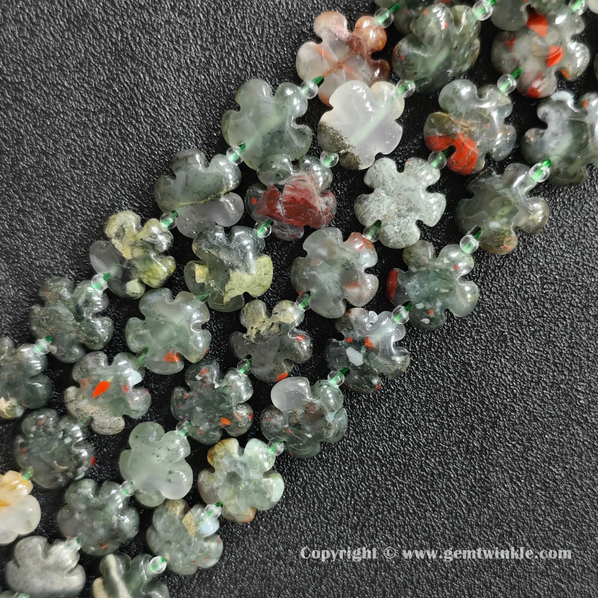 Angled view of natural African bloodstone floral carved gemstone strands laid together