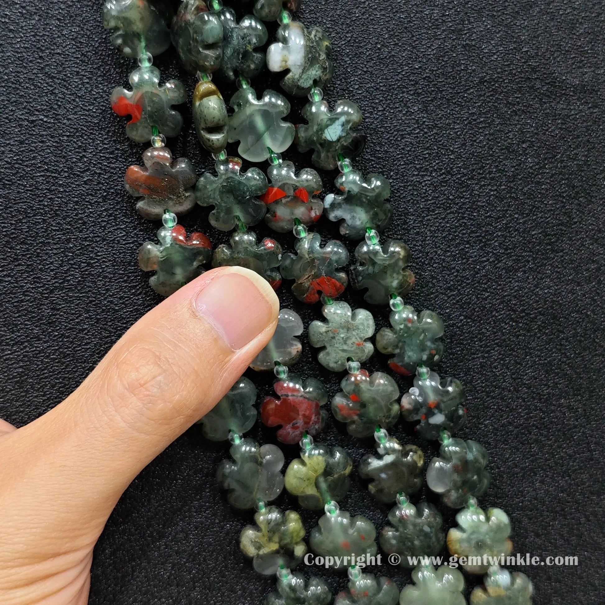 Close up view of African bloodstone plum blossom carved beads held on fingers for quality preview